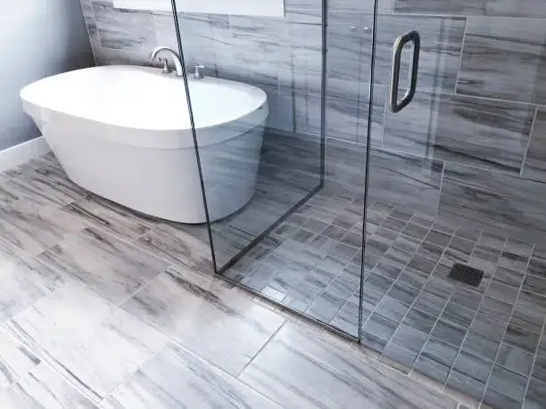 Modern bathroom with a freestanding bathtub, glass-enclosed shower, and gray tile flooring. -bathroom floor tile