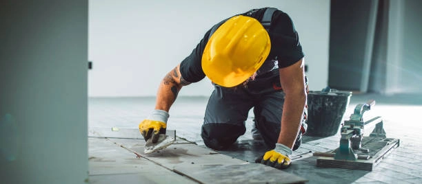 Worker in yellow helmet repairing floor tiles with precision tools. -floor repair services- Elite Remodels