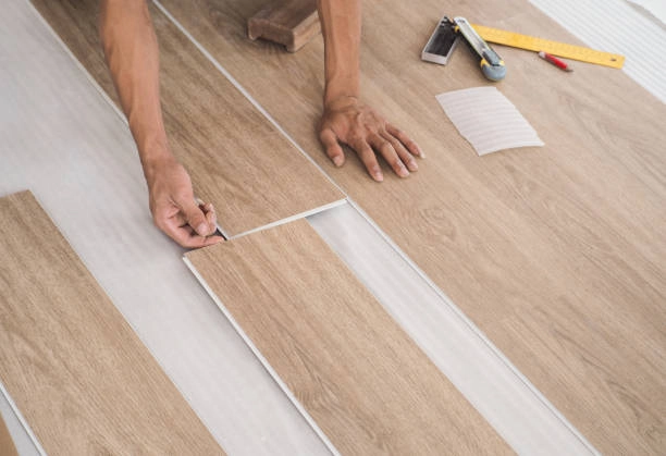 Hands installing wood-look vinyl planks with tools and precision measurement. -floor repair services- Elite Remodels